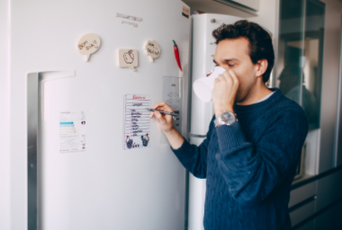 a man writing a to do list on his fridge while drinking his morning coffee